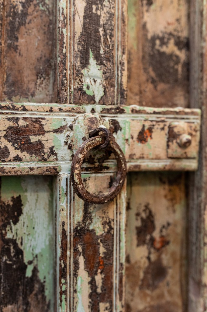Gros plan sur une poignée en anneau rouillé, fixée sur un panneau de bois à patine ancienne vert et blanc écaillé, style vintage.